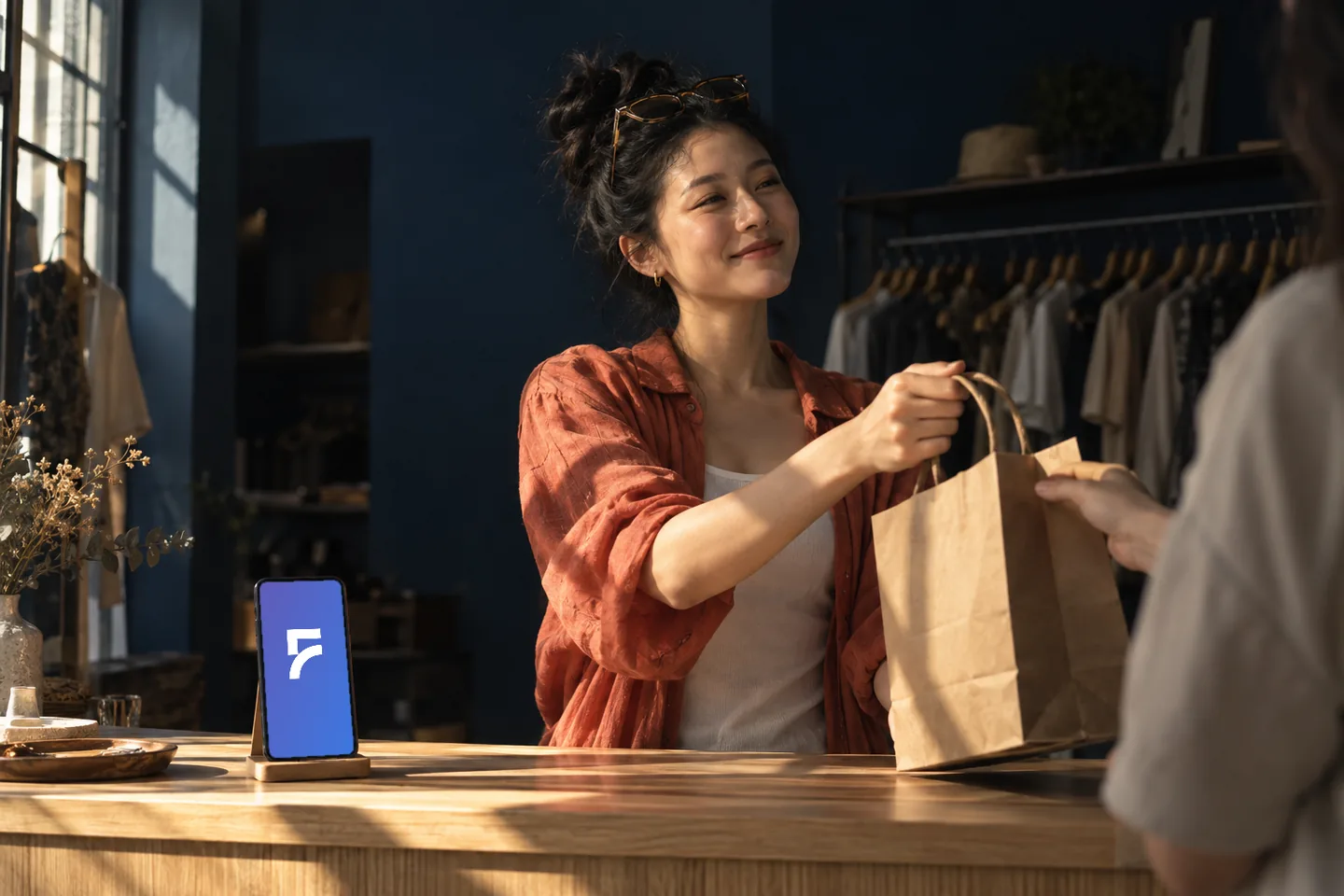 老闆娘在店裡把紙袋交給客人，櫃檯上的手機由 FRIDAI 值班