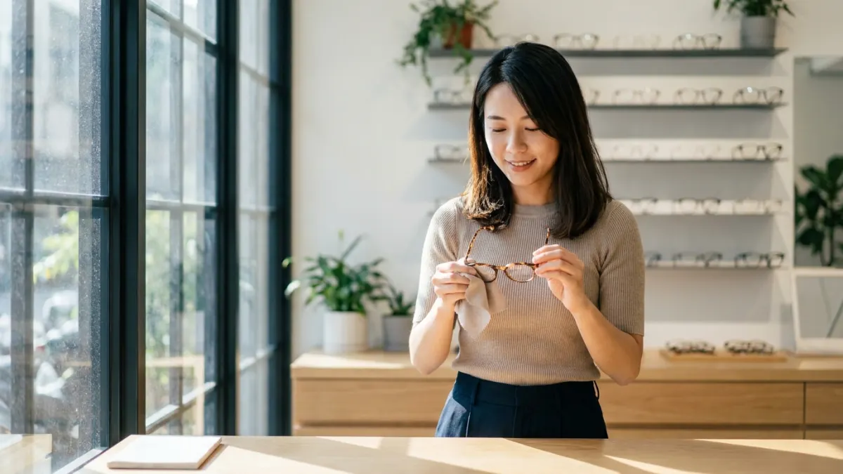 一名年輕女性在眼鏡店內，專注地擦拭一副眼鏡，神情從容而自信。